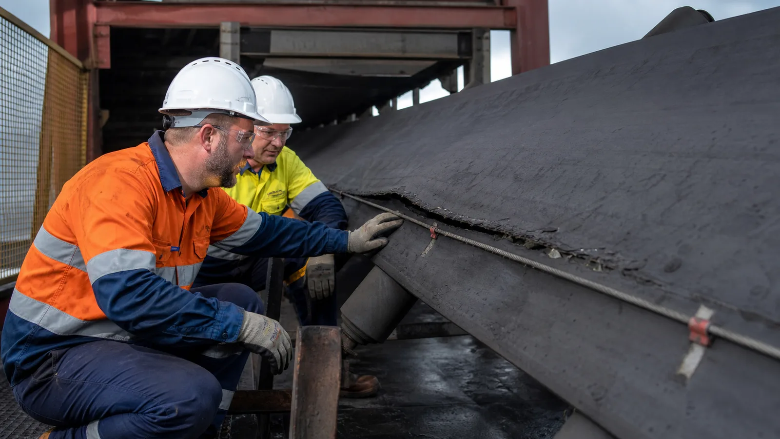 realistic damaged industrial conveyor belt being inspected near a rip detection cable